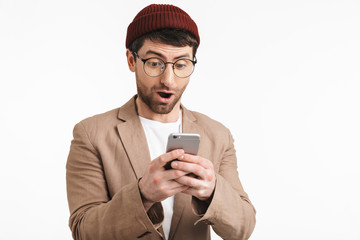 Photo of surprised man 30s wearing hipster hat smiling while holding and using smartphone
