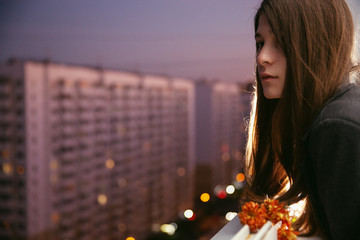 Young natural beauty long hair girl with flowers on the balcony. Spring. Evening. High-rise area. Portrait. Aesthetics