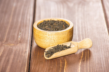 Lot of pieces of dry black tea earl grey with wooden bowl and wooden scoop on brown wood