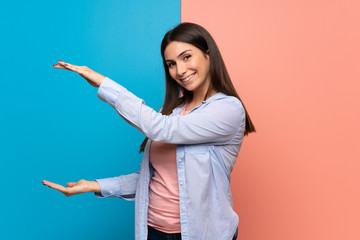 Young woman over pink and blue wall holding copyspace to insert an ad