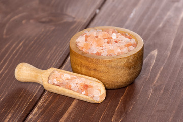 Lot of pieces of mineral pink himalayan salt crystals in a wooden bowl on brown wood