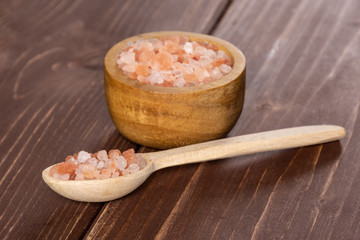Lot of pieces of pink himalayan salt crystals in a spoon on brown wood