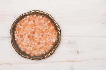 Lot of pieces of pink himalayan salt crystals in old iron bowl flatlay on white wood