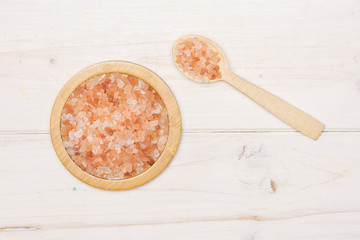Lot of pieces of pink himalayan salt crystals in a spoon flatlay on white wood