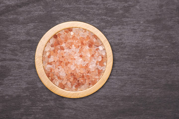 Lot of pieces of pink himalayan salt crystals on bamboo plate flatlay on grey stone