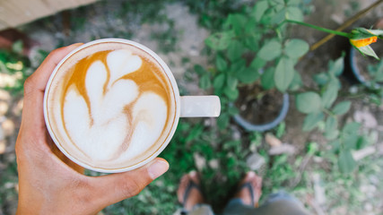 Man Hand holding cup of coffee latte art in garden at home Top view.