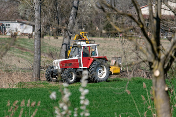 Trattore rosso e bianco che rasa erba e sponde dei campi per le coltivazioni agricole