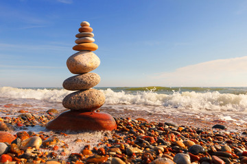 Rock zen pyramid of multi-colored pebbles in the pink rays of the setting sun against the sea. Concept of balance, harmony and meditation