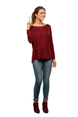 A full-length shot of a Blonde woman showing and lifting a finger in sign of the best over isolated white background