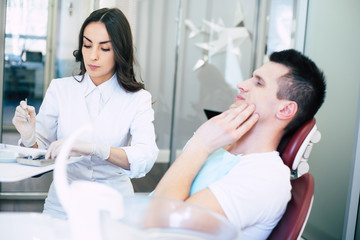 Obraz premium Periodontics. Professional doctor of dental clinic is in process of giving treatment to the patient who is having a hard pain in his teeth and it can be seen in his gestures.