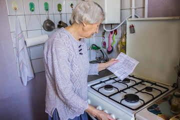 Senior old housewife at home and examines gas and electricity bills
