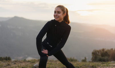 Young athletic woman stretching before intense morning workout at sunset or sunrise in beautiful mountain location