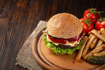 Homemade hamburger close-up with beef, tomato, lettuce, cheese and french fries on cutting board