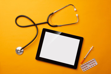 Stethoscope in doctors desk with digital tablet, syringe and pills