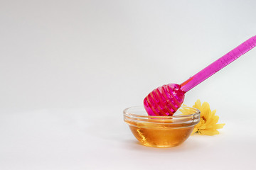 purple honey dipper picks up honey from a small glass jar on a light background