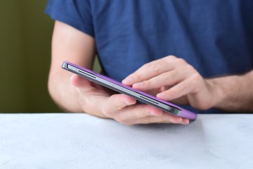 White man‘s hands holding a new tablet and put on a purple leather case with selective focus. Man using a tablet. Putting on a violet protection cases for personal tablet. Tablet accessories