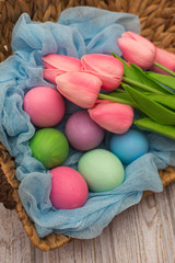 Colorful Easter eggs and pink tulips in a wicker basket on wooden background