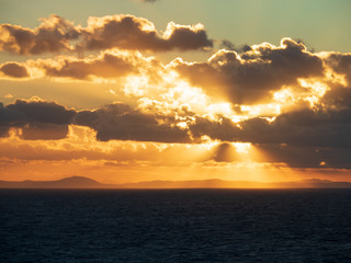 Sun rays burst out from behind clouds as the sunset over the ocean