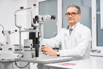 Naklejka na ściany i meble Doctor ophthalmologist posing with slit lamp in cabinet.