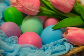Colorful Easter eggs and pink tulips in a wicker basket on wooden background