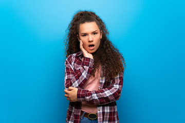 Teenager girl over blue wall surprised and shocked while looking right