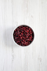 Obraz na płótnie Canvas Full bowl of dry organic cranberries over white wooden background, top view. Overhead, from above, flat lay.