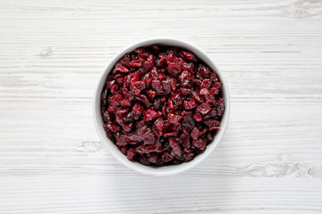 Full bowl of dry organic cranberries over white wooden surface, top view. Overhead, from above, flat lay. Close-up.