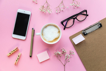 Flatlay pink background office home working space with coffee, paper holder, stickers and phone