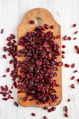 Dry raw cranberries on rustic wooden board over white wooden surface, top view. Overhead, from above, flat lay.