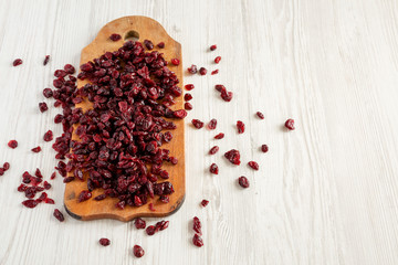 Dry organic cranberries on rustic wooden board over white wooden surface, low angle view. Copy space.