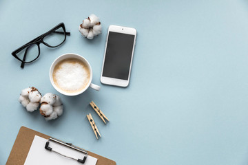 Flatlay blue background office home working space with coffee, paper holder, stickers and phone