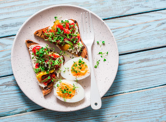 Healthy breakfast or snack - whole grain bread, feta, pickled pepper sandwiches and boiled egg on blue background, top view