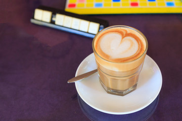 Hot Brown Caffe Latte coffee decorated with heart froth art on steamed milk foam in glass on rustic wooden table background. Espresso based coffee drink, Beverage, Afternoon drink and Caffeine Concept