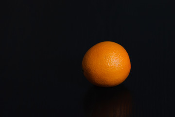 Halved and whole oranges over black background, side view. Space for text.