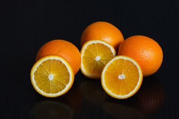 Halved and whole oranges over black background, side view. Space for text.