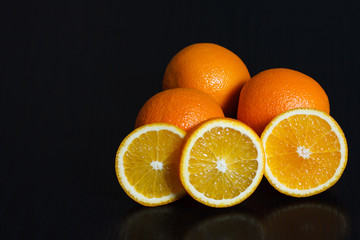 Halved and whole oranges over black background, side view. Space for text.