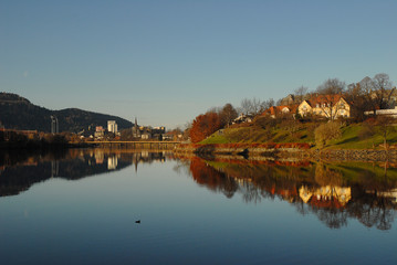 Fototapeta na wymiar Calm river, Nidelven, that flows through Trondheim City in beautiful autumn weather. The landscape is reflected in calm water.