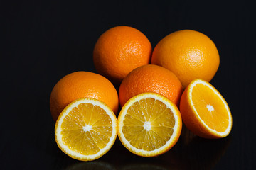 Halved and whole oranges over black background, side view. Space for text.