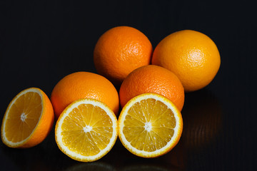 Halved and whole oranges over black background, side view. Space for text.