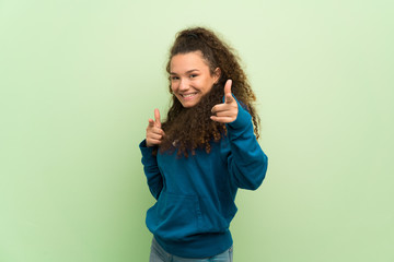 Teenager girl over green wall pointing to the front and smiling