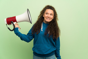 Teenager girl over green wall taking a megaphone that makes a lot of noise