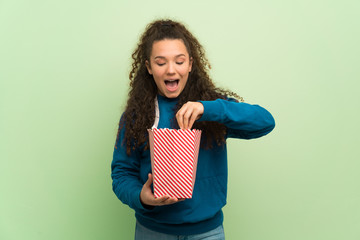 Teenager girl over green wall surprised and eating popcorns