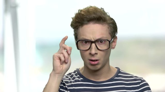 Smart boy in eyeglasses having an idea. Teen boy adjusting his glasses with thoughtful expression. Young funny genius.