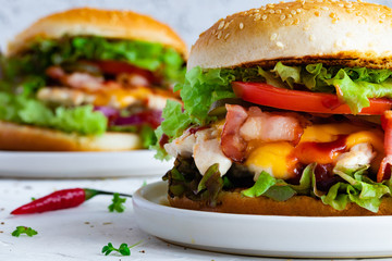 Fresh tasty chicken burger on white table. Two chickenburgers with bacon, lettuce, tomato, sauce, cheese and chili pepper, close-up