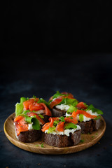 Homemade toast sandwich with rye bread, salmon, avocado, cottage cheese and microgreen sprouts on dark background. Healthy food - breakfast