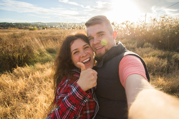 Travel, tourism and nature concept - Smiling couple taking selfie on field and showing thumbs up