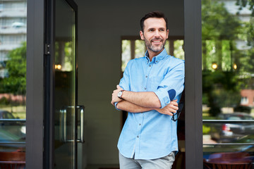 Happy restaurant owner standing at entrance looking away