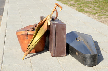 Vintage luggage items, suitcase, umbrella, hat box and musical instrument standing on a sidewalk in...