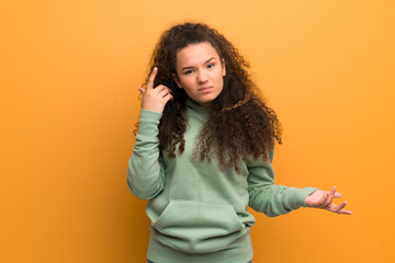 Teenager girl over ocher wall making the gesture of madness putting finger on the head