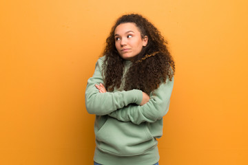 Teenager girl over ocher wall making doubts gesture while lifting the shoulders